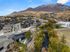 Charming aerial view of a serene residential community nestled at the base of picturesque mountains, featuring modern homes surrounded by lush nature and a calming river.