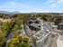 Scenic aerial view of a modern apartment complex with stunning greenery, a meandering river, and a vibrant sports court, set against a backdrop of majestic mountains.