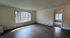 Bright and inviting living area with large windows and modern dark wood flooring, offering a seamless flow into the adjacent bedroom.