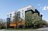 Modern apartment building with sleek architecture, floor-to-ceiling windows, surrounded by lush greenery and a clear blue sky.