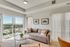 Bright living room with modern decor, large gray sofa, stylish coffee table, and floor-to-ceiling windows offering a stunning city view from the balcony.