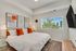 Bright and modern bedroom featuring a large bed with vibrant orange pillows, artistic wall decor, and a scenic view through a wide window.