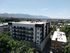 Modern urban apartment building with sleek design, surrounded by lush greenery and stunning mountain views in the background.