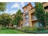 Charming apartment exterior with stone accents, lush landscaping, and inviting balconies under a bright blue sky.