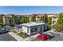 Charming apartment community with modern beige buildings, lush green trees, and ample parking space under clear blue skies.