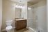Modern bathroom featuring a spacious glass shower, elegant vanity with granite countertop, and sleek tile flooring.