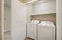 Convenient in-unit laundry area with modern washer and dryer, complemented by a neutral palette and ample shelving.