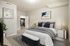 Elegant bedroom with plush bedding, modern decor, and a view into a sleek kitchen with stainless steel appliances.