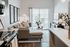 Chic and inviting open living space with modern furniture, cozy couch, decorative pillows, and large windows offering ample natural light.