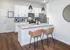 Modern kitchen in a chic apartment showcasing sleek white cabinetry, stainless steel appliances, and a stylish breakfast bar with wicker stools.
