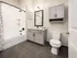 Modern bathroom featuring sleek gray cabinets, a stylish framed mirror, elegant tile flooring, and a chic subway-tiled bathtub with vibrant floral shower curtain.