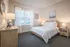 Bright and inviting bedroom with cozy decor, featuring a large window, modern wooden furniture, and elegant artwork.