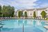 Inviting apartment complex with a large, sparkling swimming pool surrounded by modern lounge chairs and lush greenery.