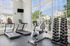 Bright and inviting gym with large windows featuring modern treadmills, an exercise bike, and a full rack of dumbbells, overlooking a serene outdoor pool and garden area.