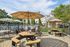 Elegant outdoor seating area with umbrellas overlooking a sparkling pool, surrounded by lush greenery and beautiful residential buildings.
