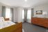 Bright and cozy bedroom featuring a modern wooden bed, elegant dresser, and soft natural light through large windows.