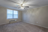 Inviting bedroom boasting plush carpet, soft beige walls, large window with natural light, and a ceiling fan for comfort.