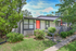 Charming mid-century modern home with vibrant front door, set amidst lush greenery and mature trees.