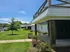 Charming apartment exterior showcasing a spacious balcony, lush green lawn, and vibrant landscaping under a clear blue sky.