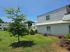 Charming suburban home with white siding, surrounded by lush green lawn and young trees under a vibrant blue sky.
