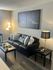 Cozy living room with a sleek black leather sofa, elegant floor and table lamps, modern art, and stylish coffee tables adorned with greenery.