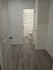 Inviting hallway with modern wood flooring leading to a bright bathroom featuring sleek white walls and blinds.