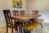 Elegant dining area with a wooden table, four chairs, and a bench, adorned with vibrant artwork and tile flooring.