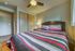 Inviting bedroom with a cozy queen bed featuring vibrant striped bedding, modern ceiling fan, and warm ambient lighting.