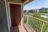 Charming apartment balcony with wooden flooring, red door, and scenic views of a vibrant neighborhood and greenery.