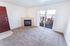 Inviting apartment living room with cozy carpet, elegant fireplace, and bright sliding doors opening to a scenic balcony view.