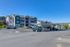 Charming apartment complex with modern design, surrounded by lush greenery and ample parking space under a clear blue sky.