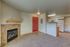 Cozy apartment interior showcasing an inviting fireplace, modern kitchen with white appliances, and plush carpeted living area.