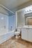 Modern bathroom with pristine white fixtures, including a bathtub, toilet, and vanity with a large mirror, over stylish tiled flooring.