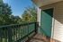 Charming balcony with green railing offering a serene view of lush trees and clear blue sky.