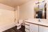 Modern bathroom with sleek white cabinetry, stylish vanity mirror, and elegant tub, featuring inviting warm tones and dark wood flooring.