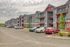 Modern multi-story apartment complex with red and gray accents, featuring private balconies and ample parking in a serene suburban setting.