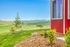 Charming countryside view from a vibrant red house with lush greenery and rolling hills under a clear blue sky.