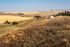 Expansive countryside view with golden fields, rustic barns, and rolling hills under a clear blue sky.