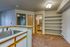 Bright, open kitchen with sleek countertops and ample shelving, adjacent to a cozy carpeted living area and modern bathroom.
