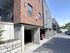 Modern apartment complex featuring red brick and gray siding with covered parking spaces, set on a sunlit street.