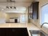 Modern kitchen with sleek dark cabinets, elegant lighting over spacious countertops, and an inviting open-concept living area with cozy fireplace and balcony access.