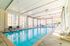 Bright indoor swimming pool area with large windows, sleek lounge chairs, and natural lighting.