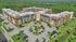 Aerial view of a modern, expansive apartment complex nestled in lush greenery, featuring ample parking and stylish architectural design.