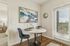 Chic dining nook with a round marble table, elegant blue chairs, and artistic wall decor, featuring a bright window view.