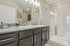 Elegant bathroom featuring dual sinks with granite countertops, modern cabinetry, and a spacious glass-enclosed shower.