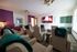 Luxurious home theater room with comfortable recliners, vibrant purple and green cabinetry, and a large wall-mounted screen displaying a cozy fireplace.