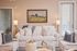 Inviting living room featuring a cream sofa with elegant pillows, warm lighting, and a charming landscape painting on a beige wall.