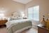 Elegant bedroom with soft beige walls, cozy floral bedding, and abundant natural light from a large window.
