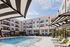 Luxurious apartment complex with modern pool area, elegant sun loungers, and stylish striped canopies under a bright blue sky.