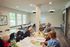 Bright and inviting community craft room with large windows, showcasing a group of smiling adults engaged in creative activities, surrounded by modern decor and uplifting atmosphere.